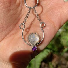 a hand holding a silver ring with a rainbow stone and amethorate on it