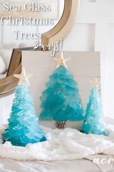 three blue christmas trees sitting on top of a white blanket in front of a mirror