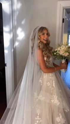 a woman in a wedding dress holding a bouquet and looking at the camera while standing next to a doorway