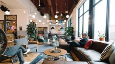 two people sitting on couches in a large living room with high ceilings and floor to ceiling windows