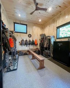 the inside of a hunting lodge with lots of coats and equipment on display, including a bench