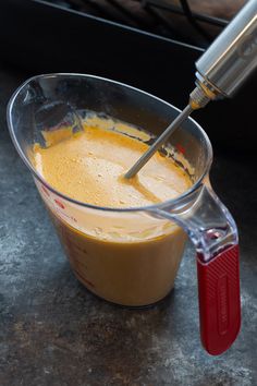 a blender filled with yellow liquid on top of a counter next to a red spatula