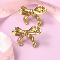 two gold bow brooches on pink fabric