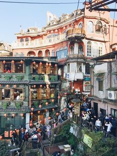 many people are standing on the side of an old building with balconies and lanterns