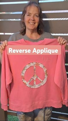 a woman holding up a pink shirt that says reverse applique with peace on it