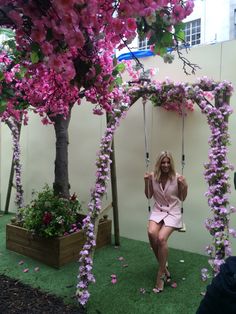 a woman sitting on a swing in front of a tree with purple flowers hanging from it