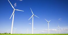 several wind turbines in the middle of a green field with blue sky and white clouds