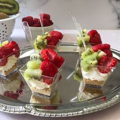 small desserts are arranged on a silver platter with strawberries and kiwi slices