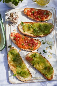 four pieces of bread with sauce and herbs on them sitting on a tray next to garlic