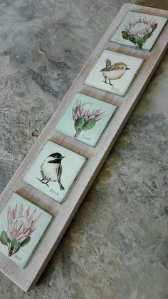 four different birds are displayed on a wooden board with flowers in the middle and one bird is sitting on top