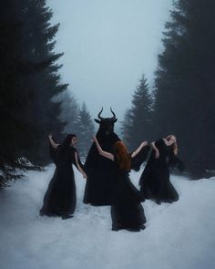 three women in black dresses are standing in the snow with horns on their heads and arms