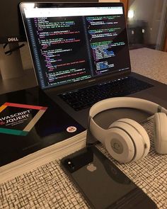 an open laptop computer sitting on top of a table next to headphones and a book