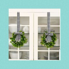 two wreaths with black and white gingham bows hang from the front of a china cabinet