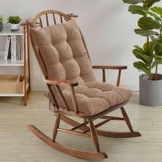 a rocking chair with a cushion on it in front of a potted plant and bookshelf