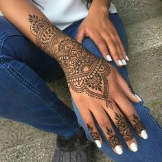 a woman sitting on the ground with her arm and hand covered in henna tattoos