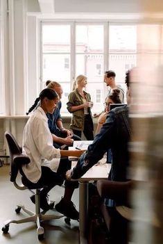 a group of people sitting around a wooden table in an office setting with chairs and desks