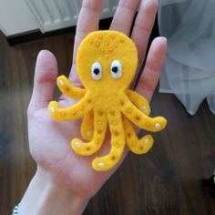 a hand holding an orange and yellow octopus toy with eyes on it's fingers