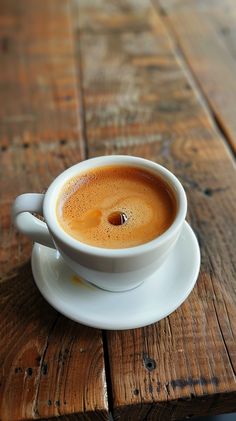 a cup of coffee sitting on top of a white saucer next to a wooden table