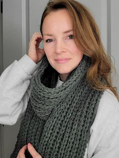 a woman wearing a gray sweater and green knitted scarf with her hands on her head