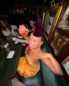 a woman wearing a party hat sitting at a table with a wine glass in her hand