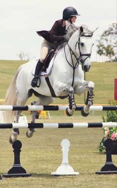 a woman riding on the back of a white horse over an obstacle