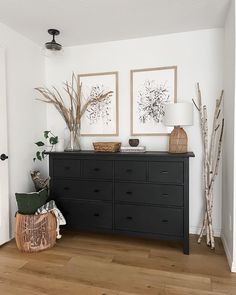 a black dresser with two pictures on the wall above it and some baskets in front of it