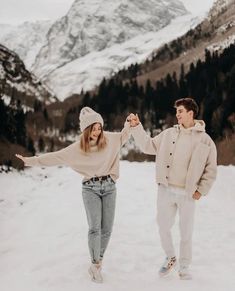 a man and woman walking in the snow with their arms around each other while holding hands