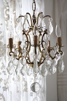 a chandelier hanging from the ceiling in front of a window with sheer curtains