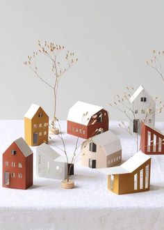 paper houses are arranged on top of a white tablecloth, with small branches in the foreground