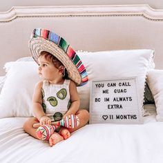 a baby sitting on a bed with a sign that says you can call me guacas