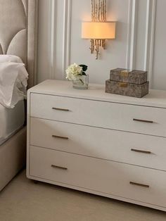 a white dresser sitting next to a bed with a lamp on it's side