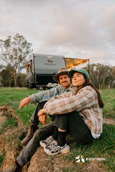 a man and woman sitting on the ground in front of an rv