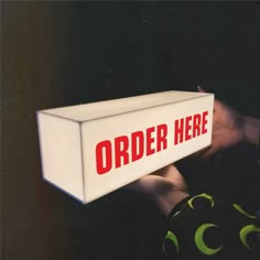 a white box with the word order here on it is held by someone's hand