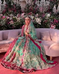 a woman sitting on top of a couch wearing a green and red wedding dress with flowers in the background