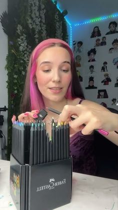 a woman with pink hair is holding a box of colored pencils