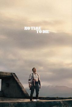 a man standing on top of a cement wall under a cloudy sky with the words no time to die above him