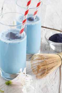 two glasses filled with blue liquid next to a whisk