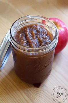 there is a jar with some food in it on the table next to an apple