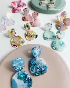 there are many different colored earrings on the plate next to each other and scattered confetti