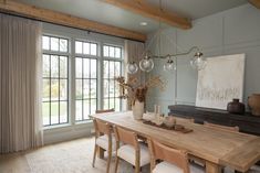 the dining room table is surrounded by chairs and vases with flowers in them, along with two large windows