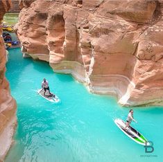 two people on surfboards in the middle of a river surrounded by rocky cliffs and canyons