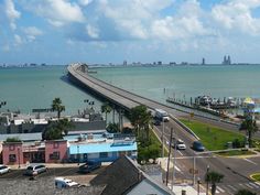 an aerial view of a bridge over the ocean with cars driving on it and buildings in the foreground