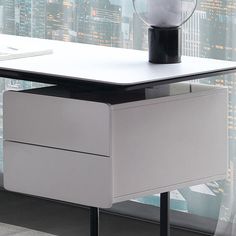 a white desk with a black top and drawers in front of a cityscape