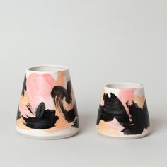 two vases sitting side by side on a white surface with black and pink designs