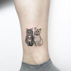 two cats tattoo on the ankle with one cat looking at the camera while the other is sitting down