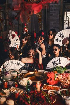 a group of people standing around a table covered in food and holding up paper fans