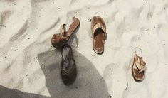 two pairs of shoes sitting on top of a white sand covered beach next to the ocean