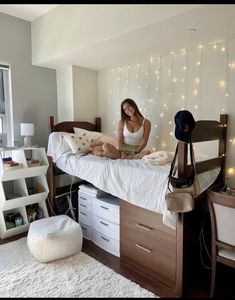 a woman sitting on top of a bed next to a white rug and lights hanging from the ceiling