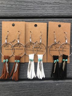 four pairs of earrings hang from hooks on a wooden surface with tags attached to them