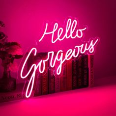 a neon sign that says hell's gorgeous on top of some books in front of a pink background